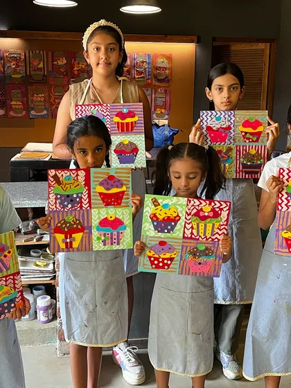 A group of girls proudly holds up their colorful cupcake pop art paintings, a fun project combining painting and collage techniques.