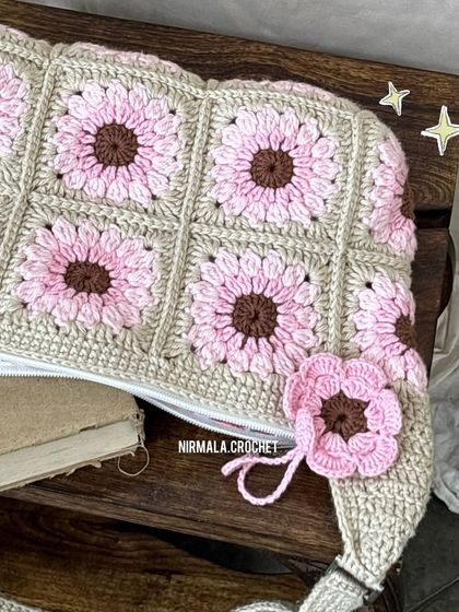 An overhead view showcasing the detailed floral granny squares and the matching flower charm on the zipper.