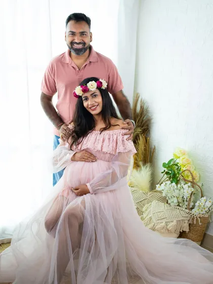 A classic couple's portrait in our bright studio. The mom-to-be is seated in a lovely pink gown while her partner stands behind her, creating a beautiful and balanced composition.