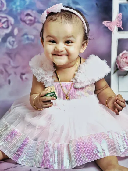 A beautiful, happy smile from a one-year-old during her butterfly-themed photoshoot. The soft pink dress and iridescent details create a magical look.