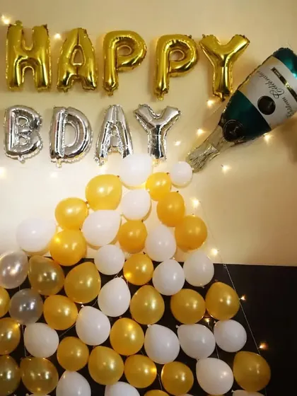 A simple and fun 'Happy Bday' wall decoration. Gold and silver foil letters are paired with a champagne bottle foil balloon pouring out white and gold balloons.