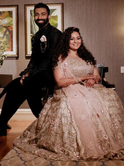 A beautiful couple posing for a portrait. The bride is wearing a heavily embellished champagne-coloured lehenga, and her makeup is kept soft and elegant to balance the look.