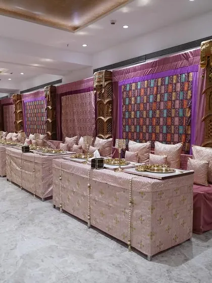 A luxurious indoor setup for a traditional event, featuring rich purple and gold fabrics, carved wooden pillars, and comfortable seating arrangements for guests to enjoy their meal.