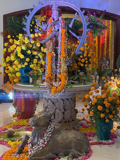 A wider view of the sacred corner, showing the Nataraja statue and the Nandi bull, both adorned with flowers. The entire installation is a beautiful tribute to tradition and artistry.