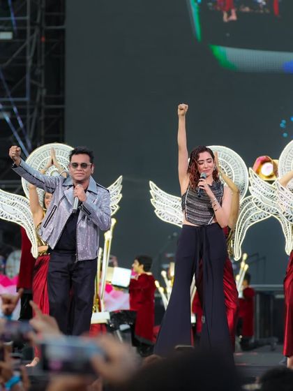 A.R. Rahman and a fellow artist raise their fists in triumph, backed by dancers with angelic wings, a testament to the powerful and visually symbolic choreography by Shiamak Davar's team.