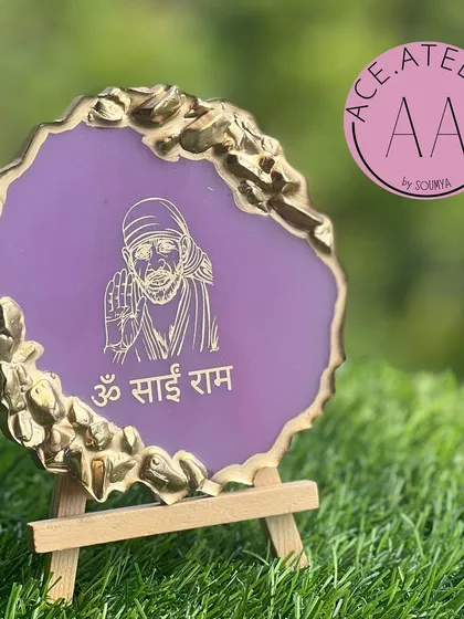 A beautiful 'Om Sai Ram' mantra frame in a calming purple with a gold geode border, resting on a wooden easel.