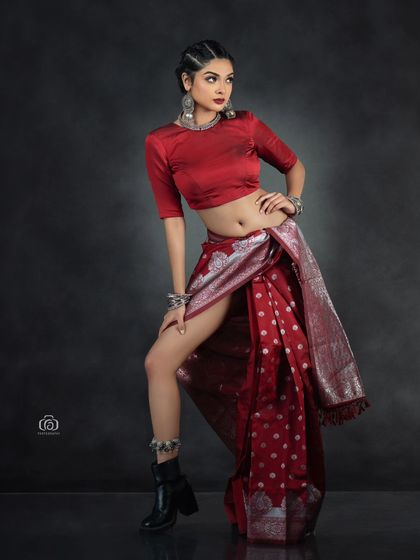 A modern fusion look, combining a traditional red saree with edgy black boots. This studio shot is about breaking conventions, using dynamic posing and strong lighting to create a powerful fashion statement.
