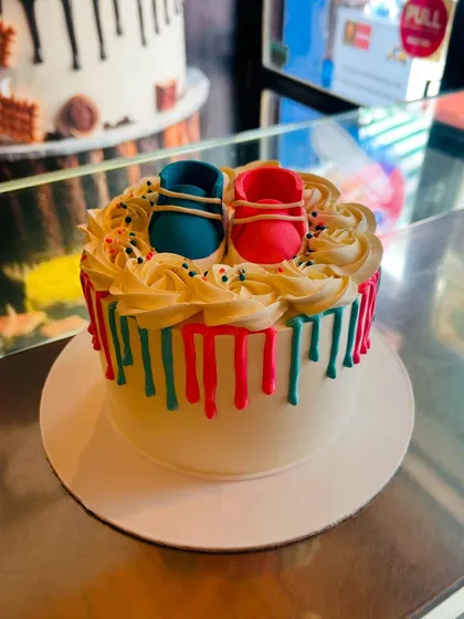 A simple yet adorable gender reveal cake with pink and blue drips and matching baby booties on top.