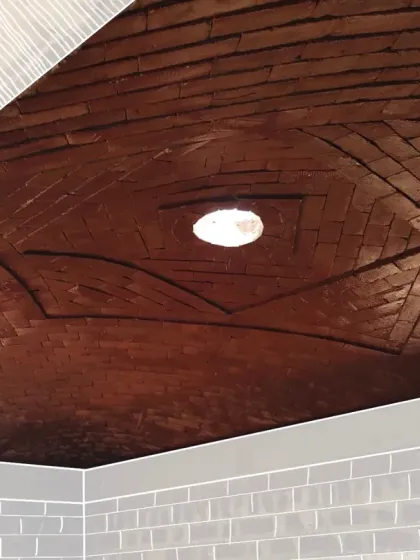 A view looking up into a completed Mexican brick dome. The alternating pattern of the bricks converges on a central keystone, creating an embracing ceiling that rests in harmony with gravity.
