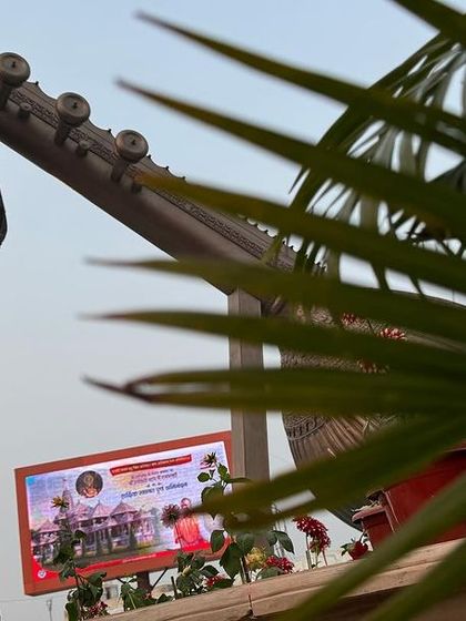 A glimpse of the massive Veena sculpture at Lata Mangeshkar Chowk in Ayodhya, framed by palm leaves. It's a beautiful tribute to art and music at the heart of a spiritual city.