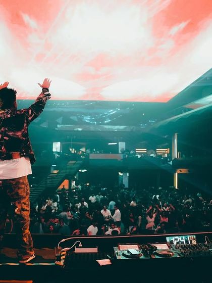 My hands up with the crowd at Quake, with a fiery visual on the screen above.