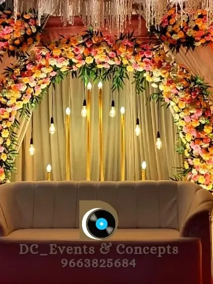 A classic Mehendi decor setup with a lush floral arch in peach and pink tones. The hanging Edison bulbs and warm uplighting create a cozy and inviting atmosphere for the ceremony.