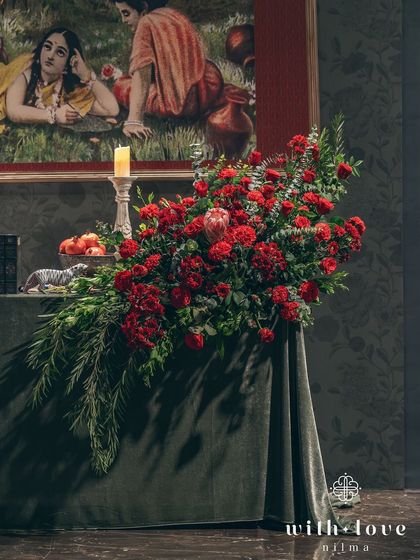 A cascading floral arrangement on a velvet-covered table. The deep reds and lush greens create a sense of opulence and drama, perfectly in tune with the artistic theme.