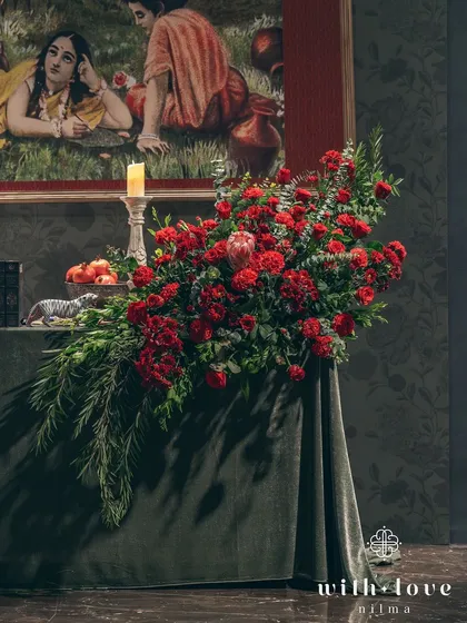 A cascading floral arrangement on a velvet-covered table. The deep reds and lush greens create a sense of opulence and drama, perfectly in tune with the artistic theme.
