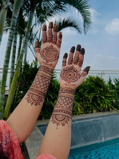 A classic and elegant design featuring a central mandala with fine, detailed work extending up the arms. The poolside setting gives it a relaxed, destination-wedding feel.