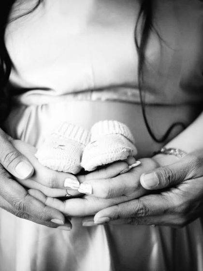 Another beautiful black and white detail shot. The focus is on the couple's hands cradling the tiny baby shoes, symbolizing the precious gift on its way.