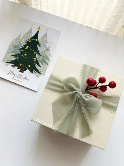 A beautifully wrapped Christmas gift box with a sage green chiffon ribbon and festive red berries.