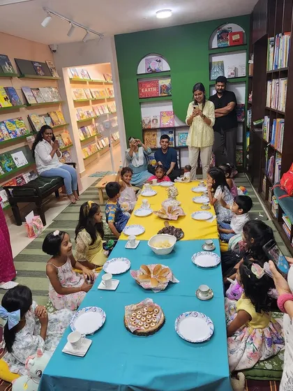 Welcome to a birthday party where stories come to life. Here, children are gathered for a delightful Mrs. Potts' Tea Party, seated at a long table surrounded by bookshelves filled with adventures waiting to be read.