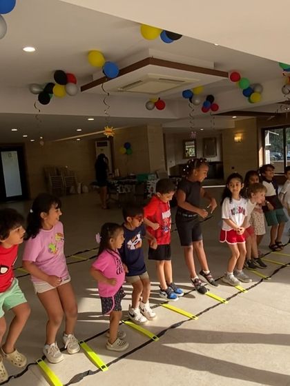 An indoor party in full swing. Kids line up for an agility ladder race in a decorated clubhouse, showing how we adapt our setup to any party venue.