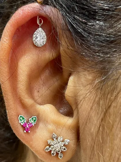 A festive Christmas-themed ear stack with holly studs and a sparkling teardrop hanging.