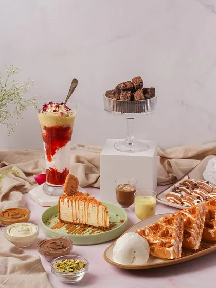 A full dessert spread featuring a cheesecake, waffles, milkshakes, and brownies. This kind of "table-scape" shot is great for showcasing the variety of a cafe's menu in a single, abundant image.