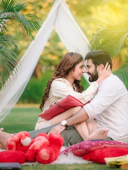 An intimate and candid moment from a romantic picnic setup on our lush green lawns. This shot captures the genuine connection between the couple, showcasing a relaxed and natural pre-wedding photography style.