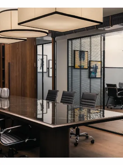The conference room in the 'Shadows' project, seen through glass partitions. The dark furniture and grey walls create a formal and modern look, while the large, custom-designed overhead lights add a sculptural element.