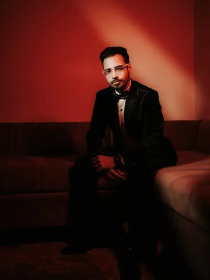A stylish portrait of the groom under a dramatic red spotlight. This moody shot highlights his sharp tuxedo and confident pose, adding a touch of cinematic flair to the wedding album.