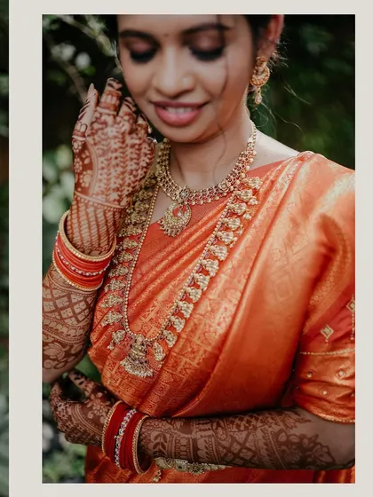 A close-up bridal portrait focusing on the beautiful details of the bride's orange saree, traditional jewelry, and intricate mehndi.