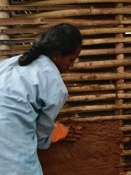 A woman mason applies daub to a wattle frame. This ancient wattle-and-daub technique uses a woven bamboo lattice filled with a mix of local clay and natural fibers. For this project, we even used upcycled dog hair for added strength and insulation.