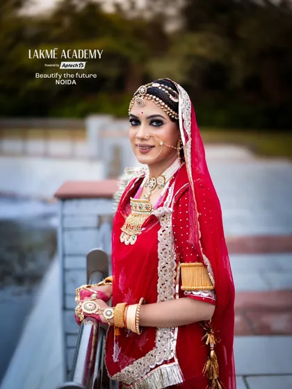 A full-length portrait of a Rajasthani bride. The vibrant red and pink attire, along with the traditional jewelry, showcases a complete look that our students learn to style.