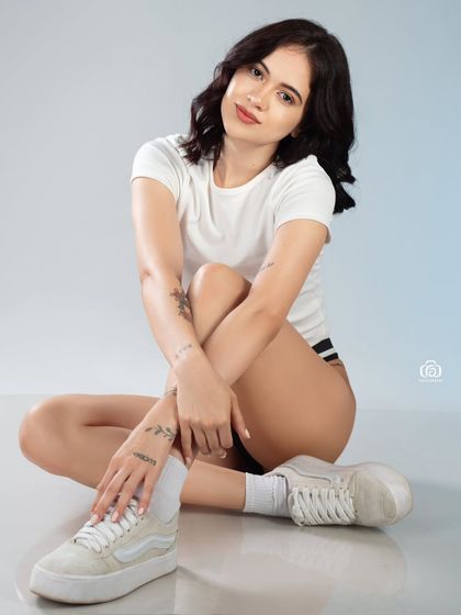 This studio shot captures a candid, relaxed moment. The simple styling with a white t-shirt and sneakers makes for an authentic and approachable portrait, great for an editorial or commercial lookbook.