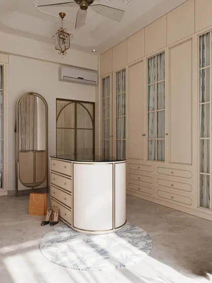 This classical dressing room features an elegant central island for accessories and ample wardrobe space with fabric-backed glass doors. The design is timeless, with a mix of curved and linear forms.