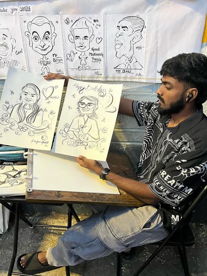 A duplicate of me at my station holding up two finished portraits.