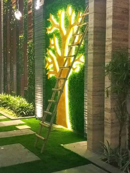 A creative and artistic green wall installation. This design features a tree silhouette created with yellow-green foliage against a darker green background, illuminated for a dramatic effect.