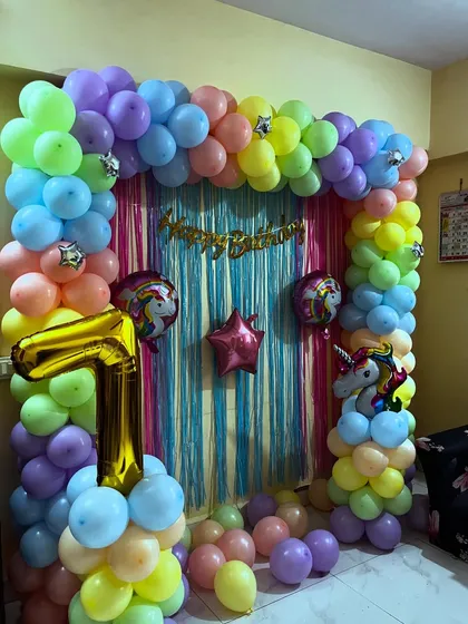 A colorful unicorn theme for a 7th birthday, perfect for a home party. The setup includes a pastel balloon arch, a shimmering backdrop, and unicorn foil balloons.