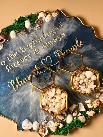For the couple who loves the sea. This beach themed engagement ring platter features real sand and seashells, with resin poured to look like ocean waves. The custom ring boxes are filled with tiny shells and pearls, making it a truly unique piece for a special day.
