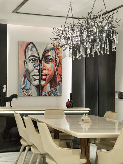 A striking dining room designed for memorable gatherings. The space is anchored by a large marble-top table, contemporary chairs, and a dramatic art piece, all illuminated by a sculptural crystal chandelier.