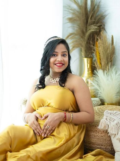 A radiant mom-to-be in a golden wrap dress, making a heart shape over her baby bump. This shot in our boho studio is full of warmth and happiness.