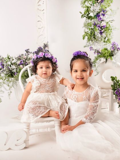 Sisters celebrating a first birthday together. The matching lace dresses and coordinated floral hairpieces make this sibling portrait extra special.