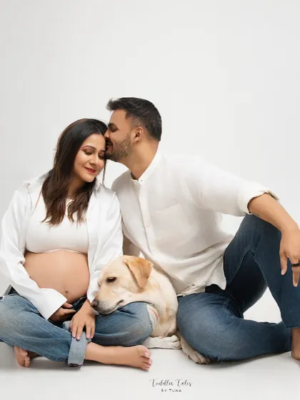 An expecting couple shares a quiet moment with their beloved dog resting its head on the mother's lap. This studio maternity portrait shows that family includes our furry members too, capturing the love that fills a home before a new arrival.