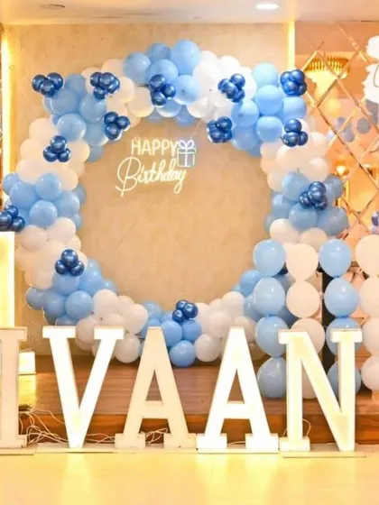 A clean and modern first birthday setup. The light-up name and circular balloon arch in shades of blue and white create a stylish and celebratory focal point on the stage.