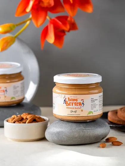 A clean and minimalist shot of Being Better's almond butter jars. The simple styling with stones and a flower gives it a natural and healthy vibe, perfect for a wellness-focused brand.