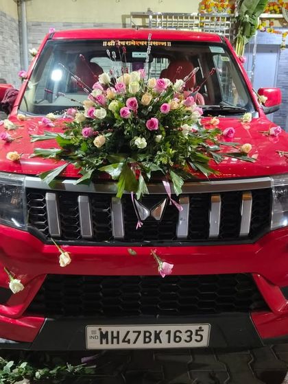 A classic bouquet of pink and white roses sits atop the bonnet of this red Mahindra Bolero. The contrast of the soft flowers against the bold red car makes for a striking image.