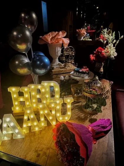 A detailed look at the personalized table setup for a birthday, featuring 'HBD JAANU' in marquee letters, a bouquet, and other decorative elements in a dimly lit, romantic setting.