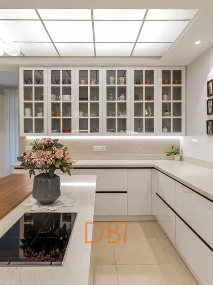 A stunning all-white kitchen with a large island and glass-fronted cabinets. The skylight and under-cabinet lighting make the space incredibly bright and airy, creating a dream kitchen for any home chef.
