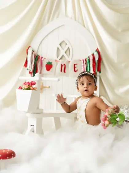 A whimsical first birthday setup with a strawberry theme, featuring a white picket fence, clouds, and mushroom props. We can bring any creative vision to life.