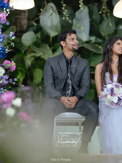 A candid moment of the bride and groom seated on their enchanted garden stage. They are surrounded by a sea of purple and blue flowers, creating a truly magical scene.