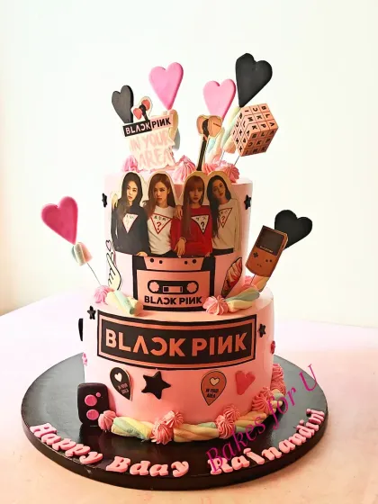 A two-tier Blackpink cake packed with fun details, including edible images of the band, marshmallows, and fondant hearts.