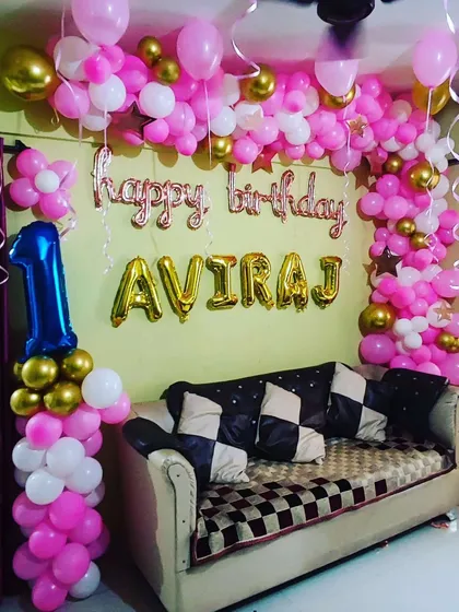 A first birthday celebration using a vibrant pink, white, and gold balloon arch. The design is personalized with the birthday boy's name in large gold foil letters.
